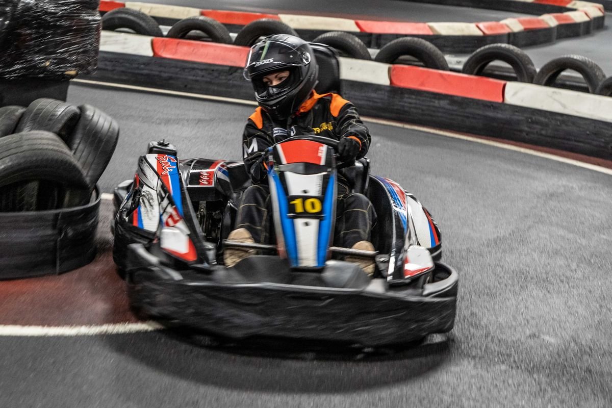 Young driver taking a corner on the indoor circuit at Teamworks Karting York, with tyre barriers on the outside of the bend